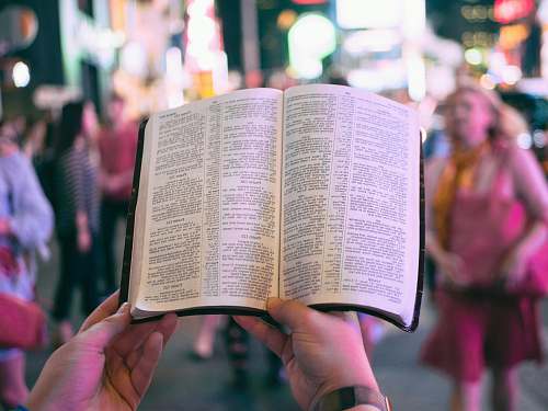 new york person holding bible on road with people walking on sidewalk beside buildings during nighttime bible